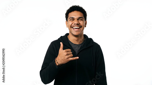 Young man with curly hair and mustache laughing and making shaka sign with hand wearing black hoodie and grey t-shirt PNG Isolated on transparent background