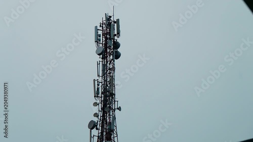 High telecommunication tower stands tall against a muted sky. Metal lattice holds many satellite dishes and antennas.