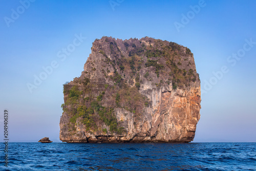 Limestone sea stack island, in the Andaman Sea, near Krabi, southern Thailand. Blue ocean in foreground; blue sky behind.
