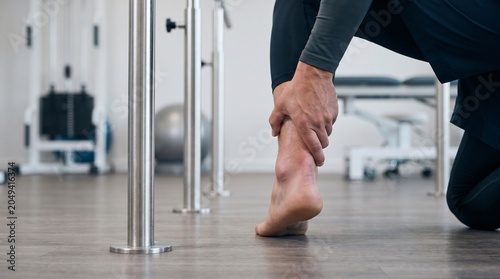 Male athlete holding swollen painful ankle in physical therapy clinic