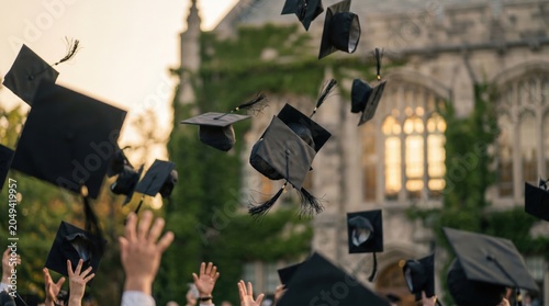 Black graduation caps being thrown into the air at university commencement ceremony with historic campus building for education milestone marketing