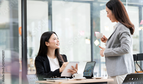 Konstfotografi Two Asian businesswomen chatting during coffee break in office.