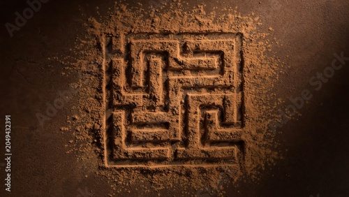 An intricate maze drawn in sand on a dark surface with a spotlight.