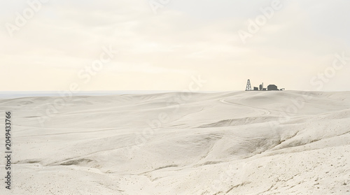 Remote industrial facility in vast white sandy desert landscape.