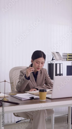 young asian woman lawyer professional writing notes reviewing legal documents working with laptop computer in modern office workspace business administration