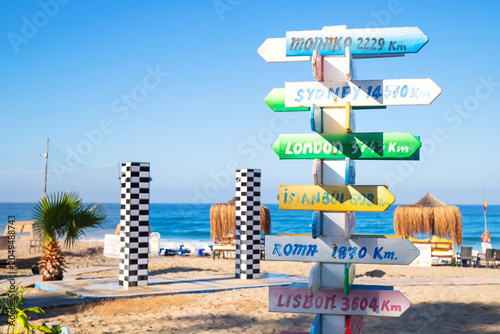 Quadro su tela Colorful direction signpost on sandy beach near the sea