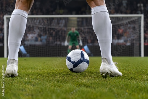 Low-angle close-up from behind the shooter’s legs moments before taking a penalty kick