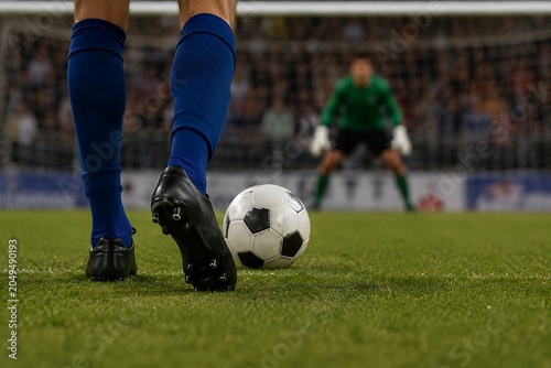 Low-angle close-up from behind the shooter’s legs moments before taking a penalty kick