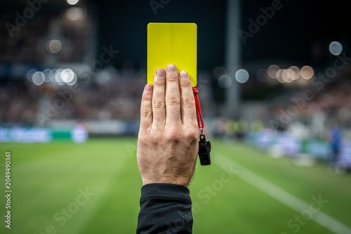 Canvastavla a referee raising a yellow card during a soccer match, whistle hanging between f