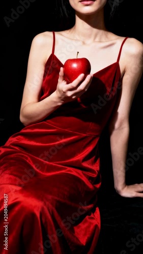 Spectacular girl in a red silk dress with an apple in her hand, seduction, sensuality, passion, attractiveness