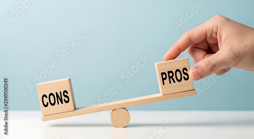 Hand balancing wooden blocks labeled 'cons' and 'pros' on a seesaw balance weighing decision choice