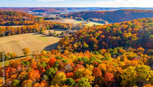 Aerial view of a stunning autumn landscape with vibrant foliage, a harvested field, and rolling hills under a clear sky