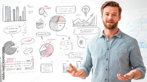 Man in casual shirt stands confidently in front of whiteboard filled with colorful charts and diagrams, presenting ideas with enthusiasm