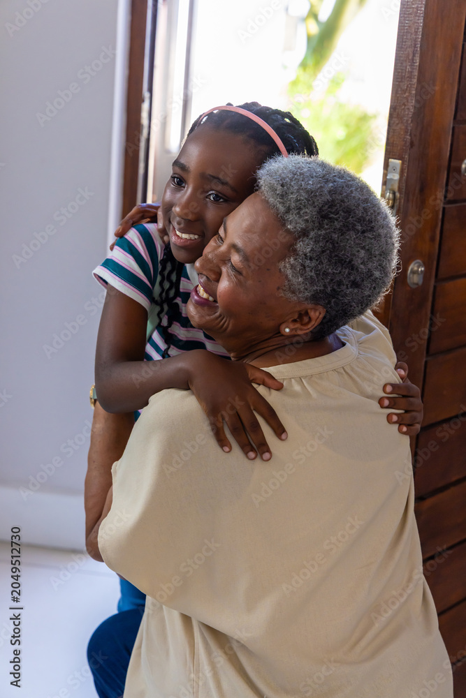 Obraz premium African American senior woman and child hugging, sharing warm embrace in doorway with wooden door