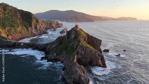 Aerial drone footage orbiting left with wide view of Gaztelugatxeko Hermitage church on rocky islet at sunset on a spring evening, Basque Country Spain
