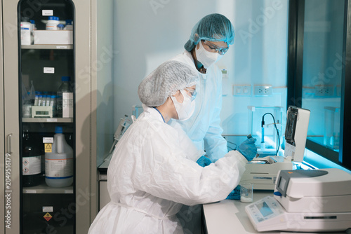 Tableau sur toile Two Asian female environmental scientists analyzing water quality samples with centrifuge and petri dish in laboratory
