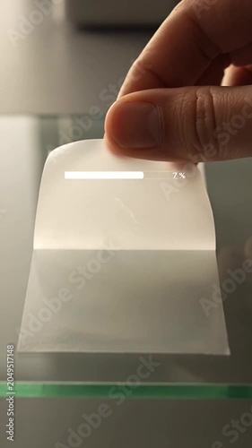 Hand peeling off transparent protective film from glass surface close up.