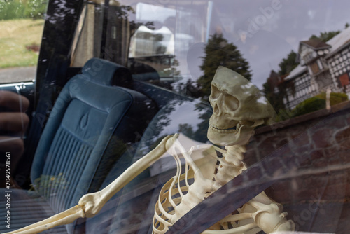 Photography Close up of a plastic skeleton sitting in the driver seat of a vintage blue vehi