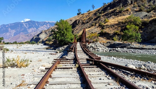 Twisted and collapsed railway tracks leading to a ruined bridge over a dry riverbed in a mountainous landscape