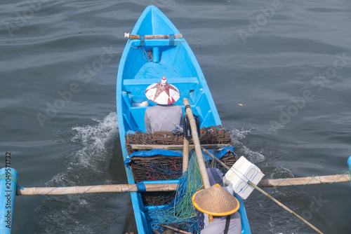 A high-angle view of fishermen aboard a traditional blue outrigger boat loaded with crab traps and fishing nets in Cilacap, Indonesia.