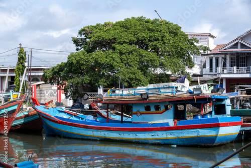 A colorful traditional wooden fishing boat docked beside a fishing village in Cilacap, Indonesia.