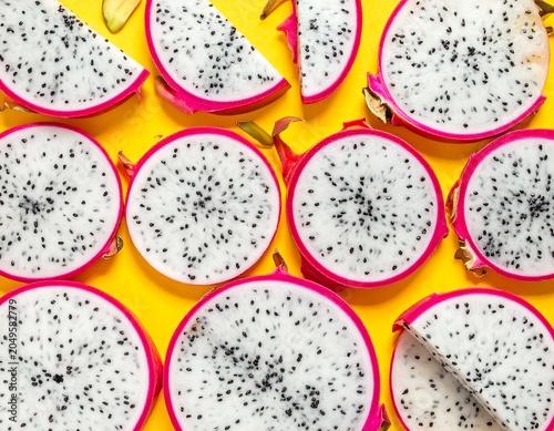Close-up vibrant shot of sliced dragon fruit on a yellow surface, showcasing white flesh and black seeds