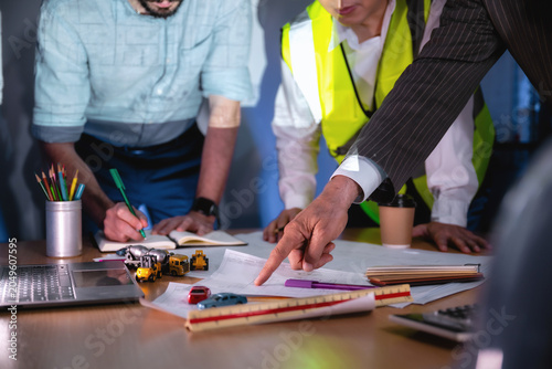 close up hand investor pointing construction blueprint boardroom meeting night, Three business people work together on a blueprint