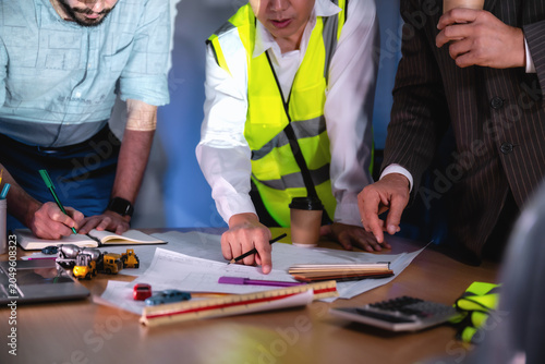 Close up hands engineers drawing blueprint construction planning boardroom night, Three workers examine a blueprint together, Three people work together at table