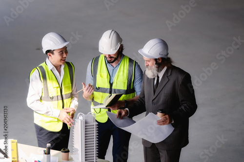 Real estate developers examining architectural model at empty space floor in building construction site, High angle view close up site managers enjoy corporate engineering team discussing project.