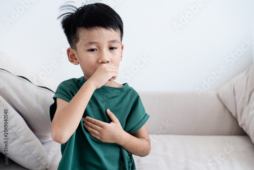 Fotografie Sick Asian little boy coughing and holding his chest on a sofa