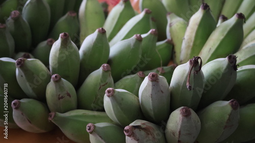 The image features a close up view of a bunch of unripe bananas. The bananas are clustered together, displaying their green skin and curved shapes
