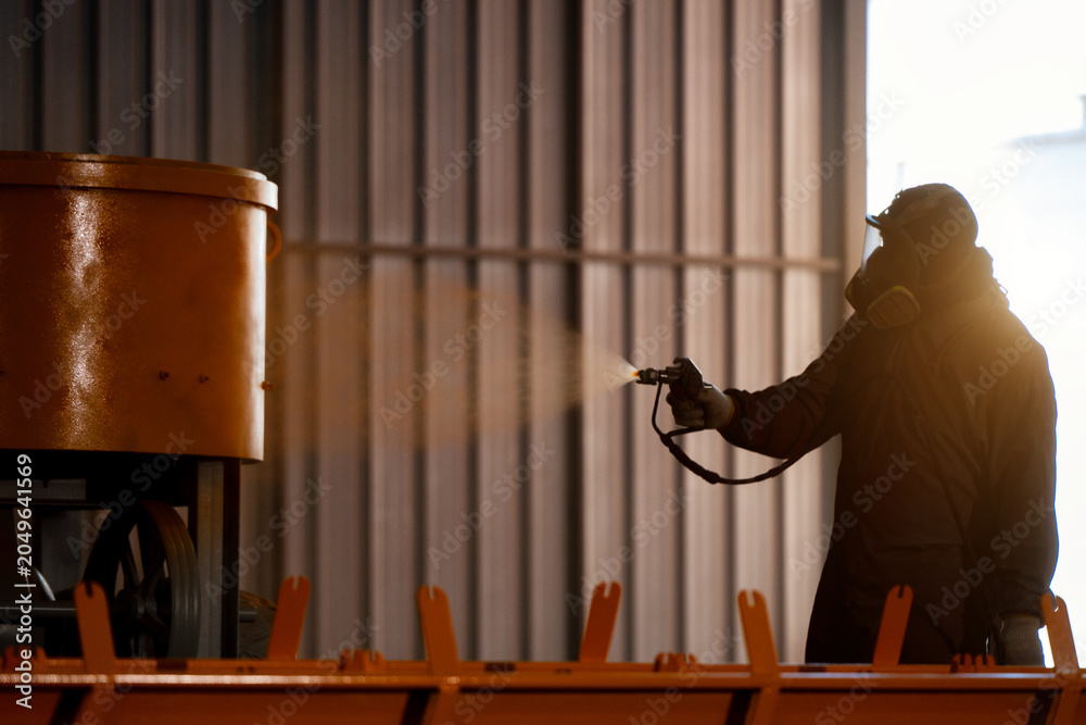 Obraz premium Industrial painter spray painting yellow coating on machinery metal parts, waring protective suit respirator mask spray painting yellow coating heavy machinery metal equipment factory workshop.