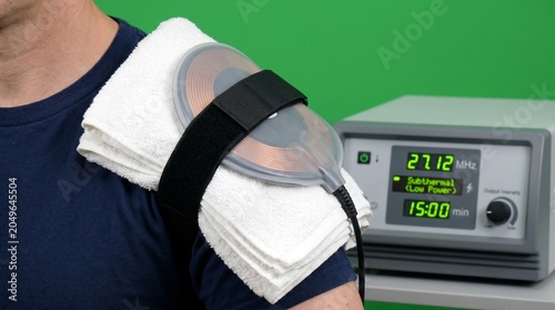 Medical professional applying shortwave diathermy treatment on patient's shoulder in clinical setting