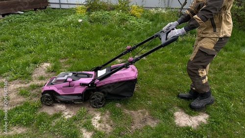 Person operating a walk-behind lawn mower while mowing grass in a garden. Upper body only, no face visible. Lawn care, backyard maintenance, landscaping, gardening and outdoor work.