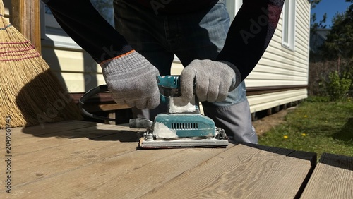 Hands in protective work gloves using an electric sander on a wooden surface during home renovation. DIY woodworking, cottage repair, construction, craftsmanship and industrial work.