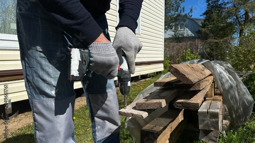 Hands in protective work gloves using a power drill on a wooden surface during home renovation. DIY woodworking, cottage repair, construction, craftsmanship and industrial work.