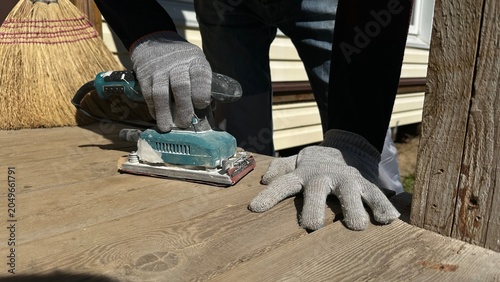 Hands in protective work gloves using an electric sander on a wooden surface during home renovation. DIY woodworking, cottage repair, construction, craftsmanship and industrial work.