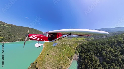 aerial footage, dynamic selfportrait of light airplane flying at low altitude over turquoise lake in a norrow valley of the french alps under blue sky 