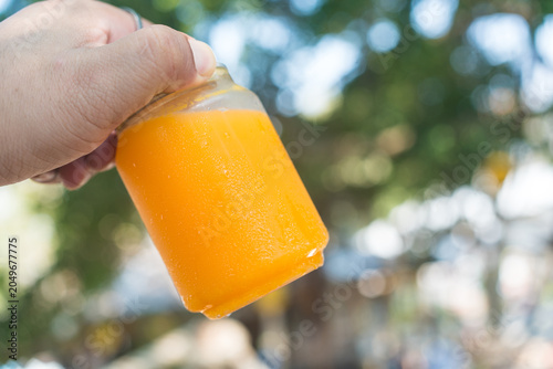 Man hand holding a can with a ring pull tab lid filled with orange juice against nature background. Summer drink