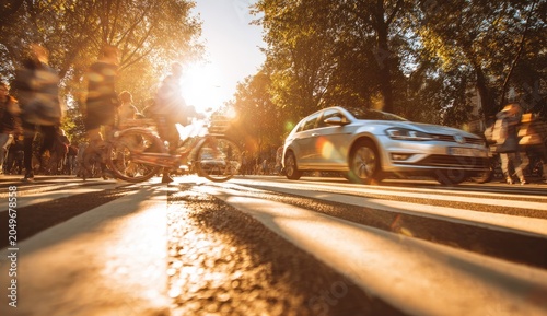 A sunlit crosswalk scene with blurred figures, a car, and bicycles at sunset