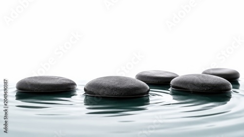 Zen basalt stones in rippling water, smooth black spa pebbles on white background, tranquil meditation concept for wellness and massage therapy