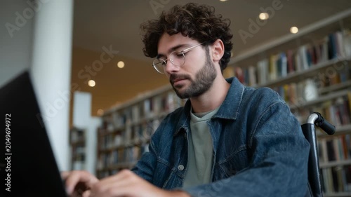 Young Man in Wheelchair Studying on Laptop in Library Setting