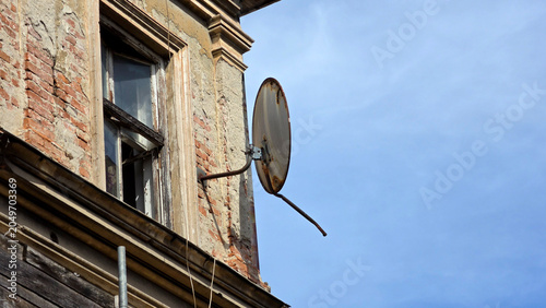 Schilderij op canvas Rusty parabolic satellite dish antenna mounted on a weathered brick building fac