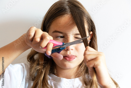 Photos A young girl with a focused expression uses scissors to cut her long brown hair