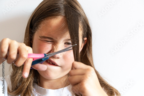Tablou pe pânză Close up of a young girl cutting her own hair with scissors