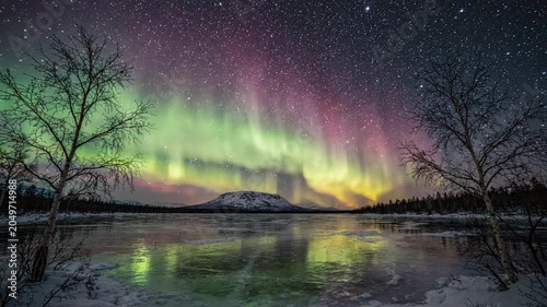 Stunning aurora borealis northern lights over a frozen lake with trees and starry sky in winter landscape