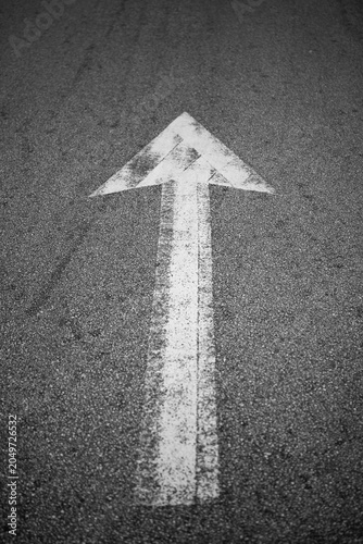 White directional arrow painted on asphalt road surface, symbolizing forward movement, direction, navigation, progress, and transportation concepts