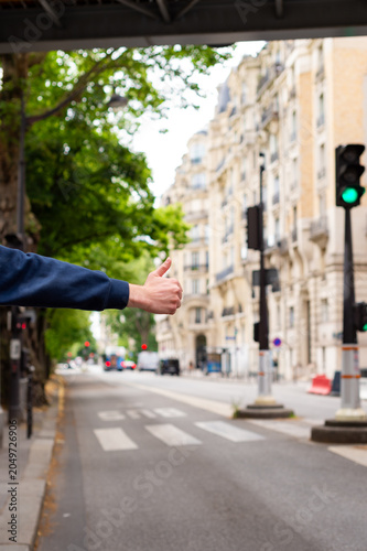 Konstfotografi A man's arm extends from the side showing a thumbs-up gesture to hitchhike or hail a ride on a Paris street
