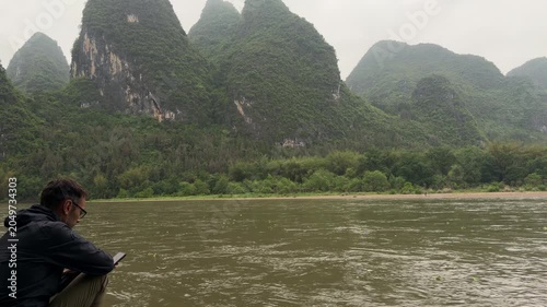 Tourist using smartphone on riverbank with karst mountains landscape in Yangshuo, China