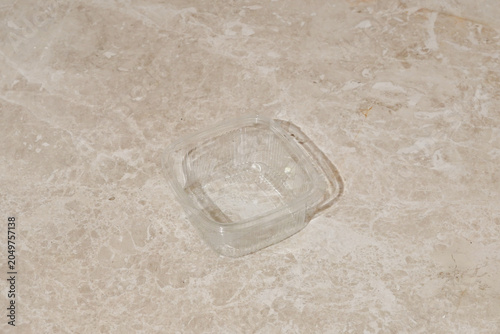 Φωτογραφία An empty, transparent, single-use plastic food container sits on a beige marble surface